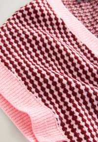 Pletený šál v růžové a burgundské barvě s vzorem houndstooth. Má žebrovaný okraj na spodní části, což vytváří texturu a kontrast.