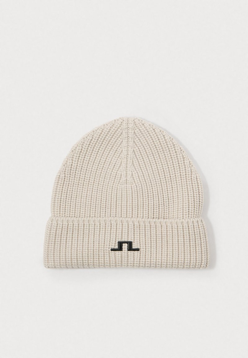 Knit beanie in light beige with a ribbed texture. Features a folded cuff and a small black logo on the front.