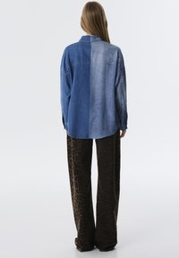 Camisa de denim con diferentes tonos de azul, con un corte relajado y pantalones de pierna ancha con estampado de leopardo marrón. Textura suave y puños abotonados.