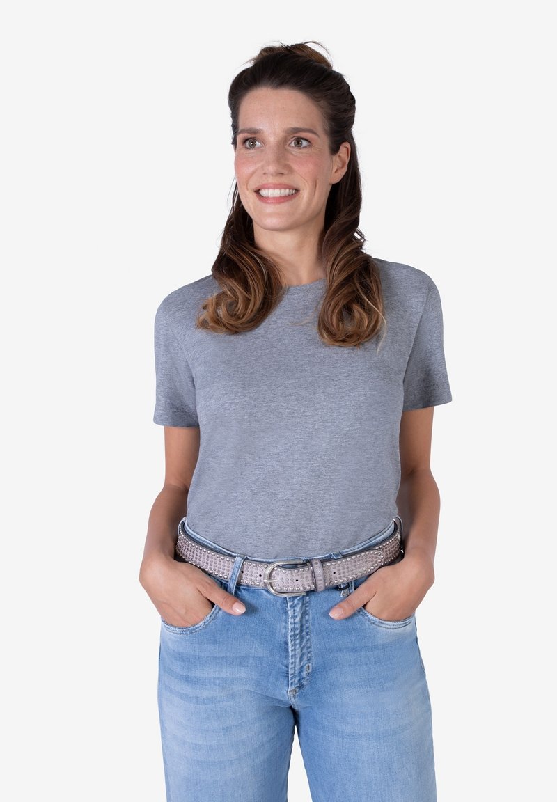 Camiseta gris de manga corta hecha de tela suave, combinada con jeans de mezclilla azul claro y un cinturón plateado con tachuelas. Corte casual con un escote redondo.