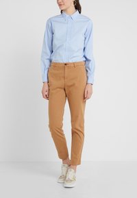 Ljusblå långärmad skjorta med knäppning, kombinerad med beige chinos. Vita och beige sneakers med snörning och gulddetaljer.