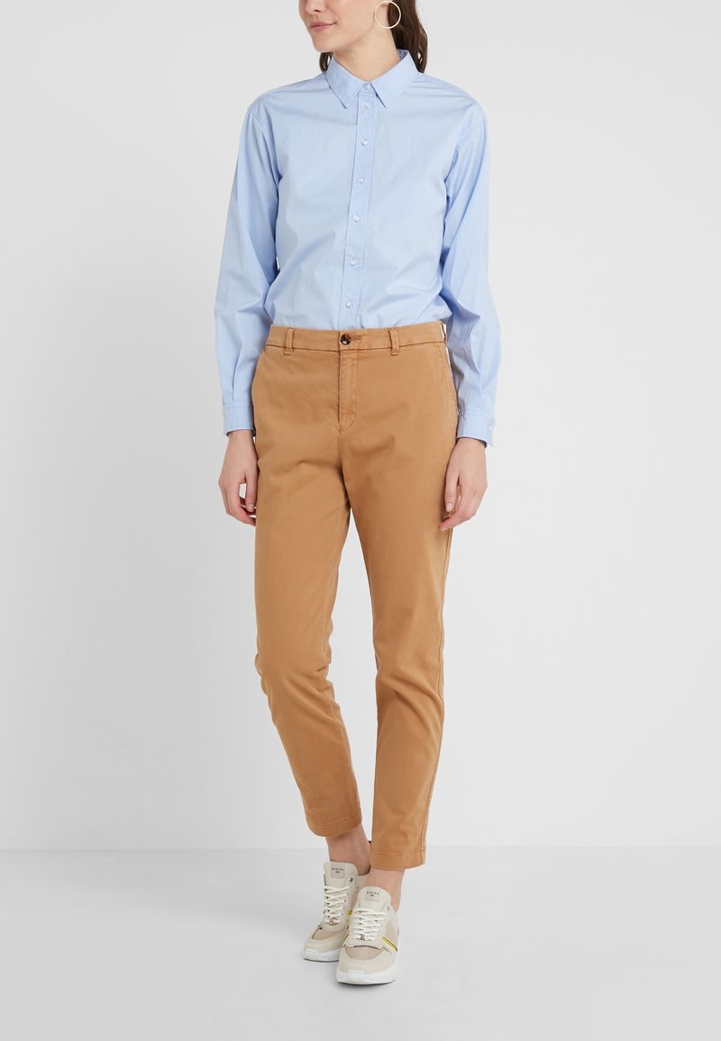 Ljusblå långärmad skjorta med knäppning, kombinerad med beige chinos. Vita och beige sneakers med snörning och gulddetaljer.