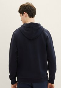 Felpa con cappuccio blu navy in tessuto morbido, con polsini e vita a coste. Presenta una vestibilità classica, con cuciture visibili sulle spalle.
