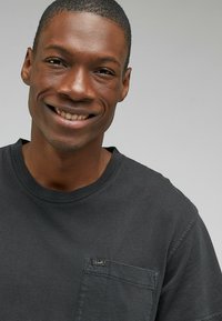 Svart bomull t-shirt med rund halsringning, korta ärmar och en bröstficka med en liten varumärkesetikett. Slät textur.