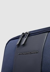 Borsa a tracolla blu navy con tessuto strutturato e dettagli in pelle liscia, dotata di doppia cerniera e logo inciso sulla parte anteriore.