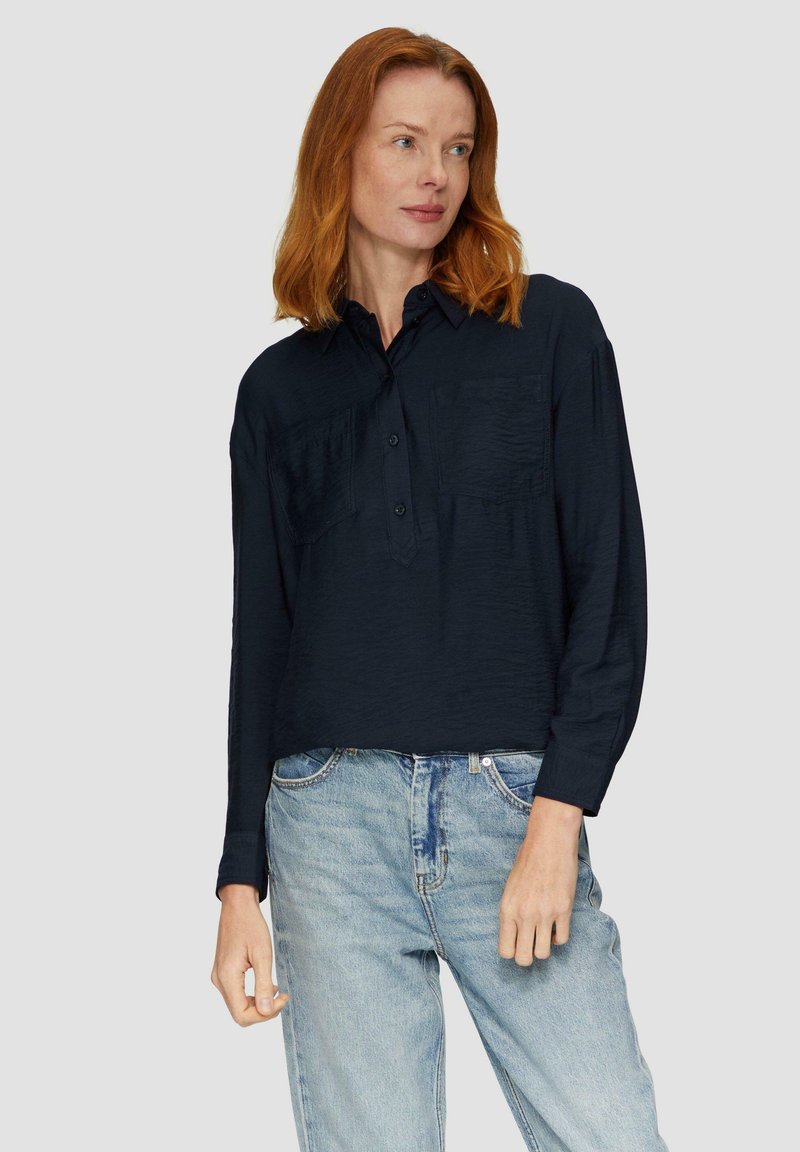 Dunkelblaue Hemdbluse mit langen Ärmeln, zwei Brusttaschen und strukturiertem Stoff, kombiniert mit hellblauen, hoch taillierten Jeans.