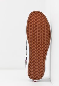 Semelle de chaussure avec motif gaufré en caoutchouc marron, semelle intermédiaire blanche et côté présentant un motif à damier multicolore sur la tige.