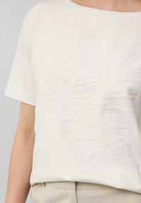 Witte t-shirt met korte mouwen, voorzien van tekstuurlijke borduursels van bladdesigns met pailletten, die het zachte materiaal en de casual pasvorm aanvullen.