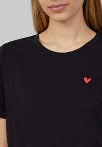 Czarny bawełniany t-shirt z małym logo czerwonego serca po lewej stronie klatki piersiowej oraz klasycznym okrągłym dekoltem.