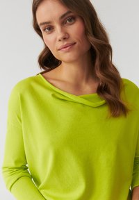 Limonengrüner Strickpullover mit einem Schalkragen und langen Ärmeln. Weiche Textur, lockere Passform und minimale Nähdetails.