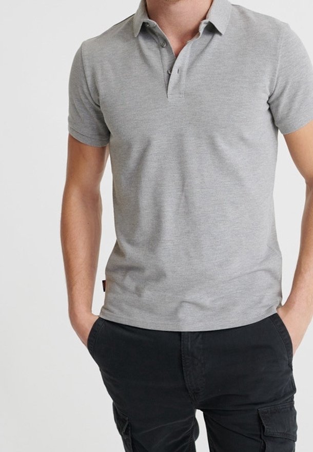 Homme portant un polo gris clair à manches courtes et un pantalon cargo noir, les mains dans les poches, sur un fond uni.