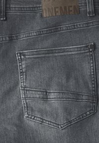 Tämä on tummanharmaat farkut, joissa on takatasku. Kangas näyttää hieman tekstuurilta, ja sen yläpuolella on ruskea nahkapatchi.