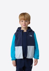 Polár cipzáras mellény tengerészkék, világoskék és élénk kék színekben. Kapucnival, elülső zsebekkel és kontrasztos színblokkokkal rendelkezik. Simogató tapintású anyag.