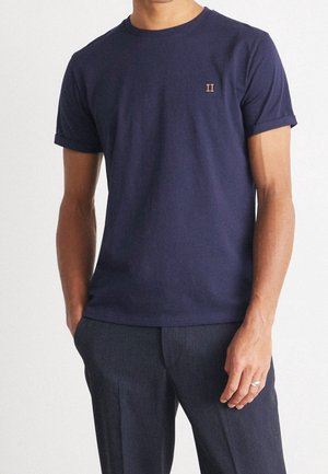 Man wearing a dark navy blue short-sleeve t-shirt with small orange "II" logo on chest, paired with dark blue pants.