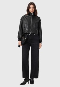 Giacca corta in pelle nera con colletto alto, chiusura con zip e tasche laterali, abbinata a jeans neri larghi e stivaletti con tacco.