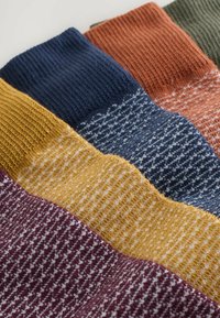 Calcetines de lana en cuatro colores (burdeos, amarillo, marino, naranja quemado) con puños acanalados, que presentan patrones de texturas variadas y un material suave.