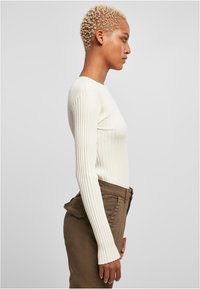 Long-sleeve white ribbed top paired with olive green pants, featuring a high waist and side pockets. The texture is soft, and the fit is close.