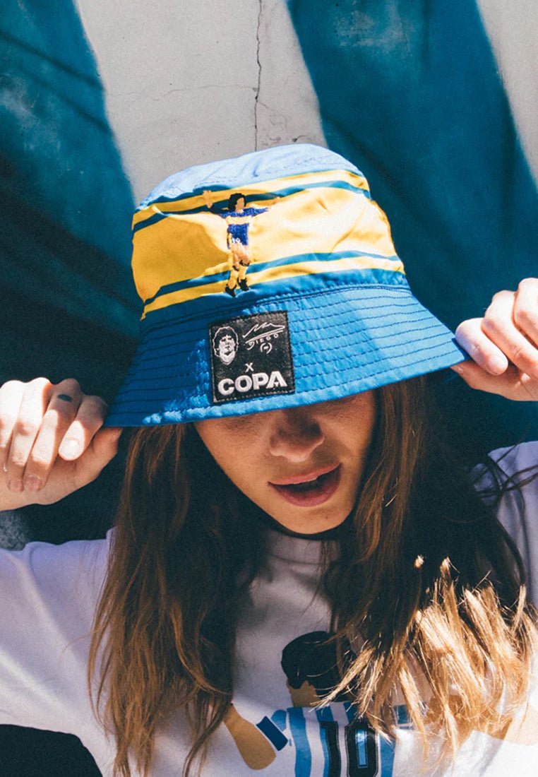 Blauw en geel emmerhoed van een gestructureerde stof, met een centraal logo-patch en borduurdetails bovenop.