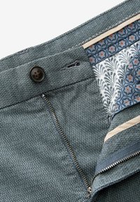 Pantalons en tissu texturé gris avec un bouton noir, fermeture éclair, et une doublure intérieure à motif floral en bleu et orange.