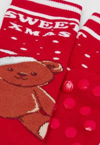 Røde strikkede sokker med et brunt bjørnedesign, hvide snemænd, teksten "SWEET XMAS" og pink gummidupper på sålen for bedre greb.