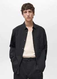 Schwarze, zerknitterte Knopfhemd mit einer einzelnen Tasche, darüber getragen ein hellbeiges Henley. Kombiniert mit schwarzen Hosen und einem Gürtel.