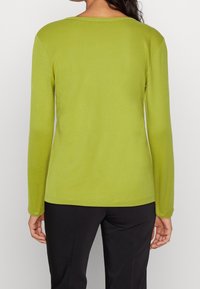 Top a maniche lunghe di colore verde lime realizzato in un tessuto morbido. Presenta un colletto rotondo e una silhouette aderente, abbinato a pantaloni neri.