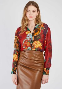 Rote Bluse mit Blumenmuster, langen Ärmeln und Knopfleiste, kombiniert mit einem engen braunen Lederrock, der glatte Texturen zur Geltung bringt.