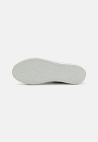 Semelle de sneaker blanche avec un motif texturé et ondulé et une marque. Bords renforcés et finition lisse. Design minimaliste sans inscriptions visibles.