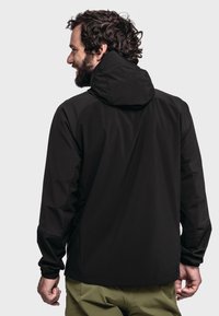 Schwarze Outdoor-Jacke mit Kapuze, schlankes Design, weiche Textur und eng zulaufende Ärmel, kombiniert mit olivgrünen Hosen.
