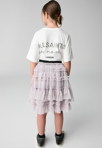Vit t-shirt med "ALLSAINTS" tryckt i nitar, ihopparad med en lager-på-lager lavendelfärgad tyllkjol med elastisk midja och svarta högra sneakers.