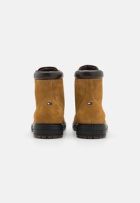 Bottines en suède marron avec un col en cuir noir, dotées d'une semelle en caoutchouc texturé et d'un petit patch logo à l'arrière.