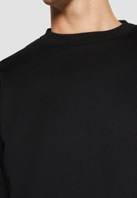 Suéter negro de cuello redondo en una tela suave y lisa. Presenta un cuello acanalado y un diseño minimalista que deja al descubierto solo una parte de la parte superior del pecho.