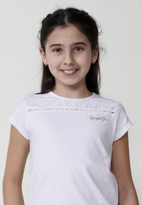 Biela bavlnená tričká s krátkymi rukávmi, s čipkovým detailom na golieri a zlatým logom "Koroshi Girl" na ľavej hrudi.
