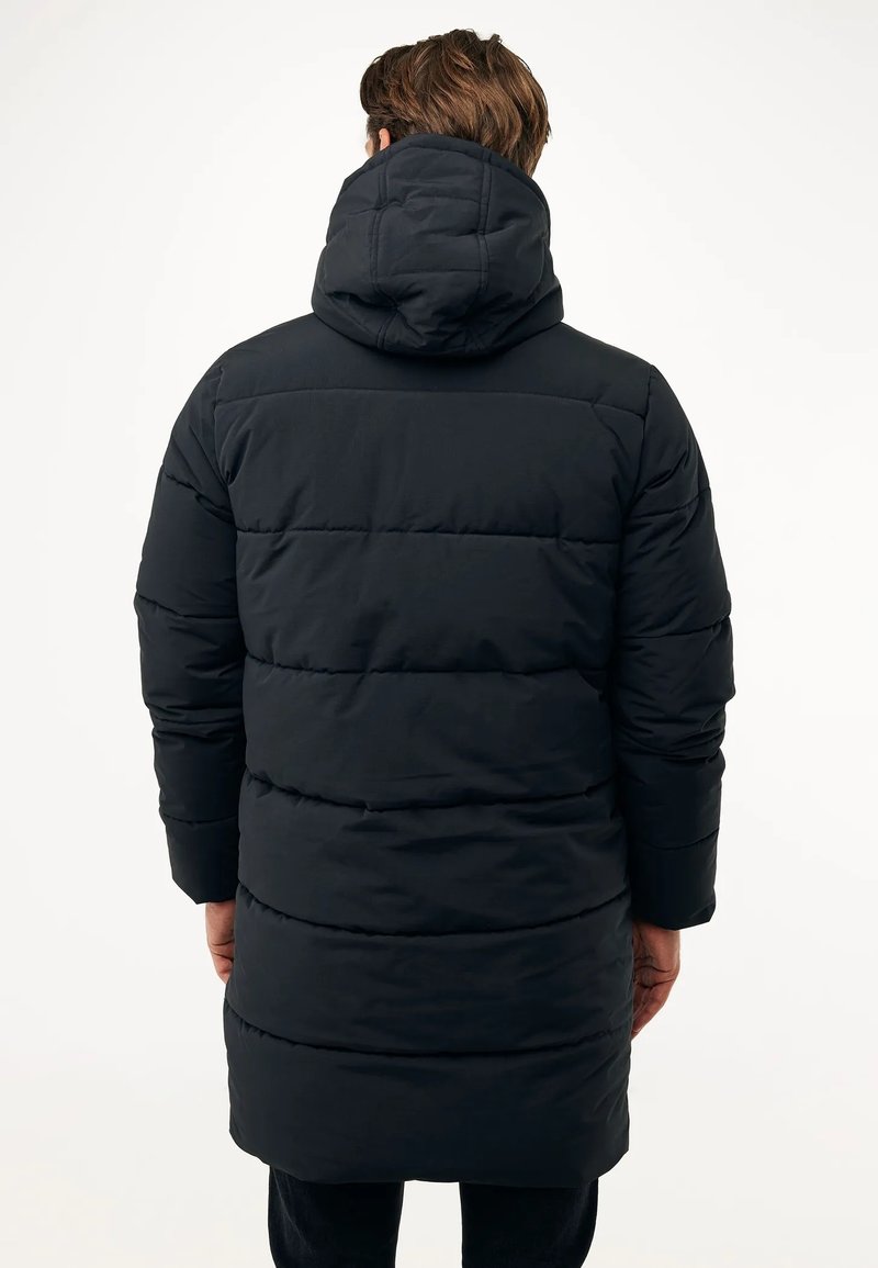 Mann, der eine lange, schwarze Daunenjacke mit Kapuze trägt, von hinten vor einem schlichten weißen Hintergrund gezeigt.