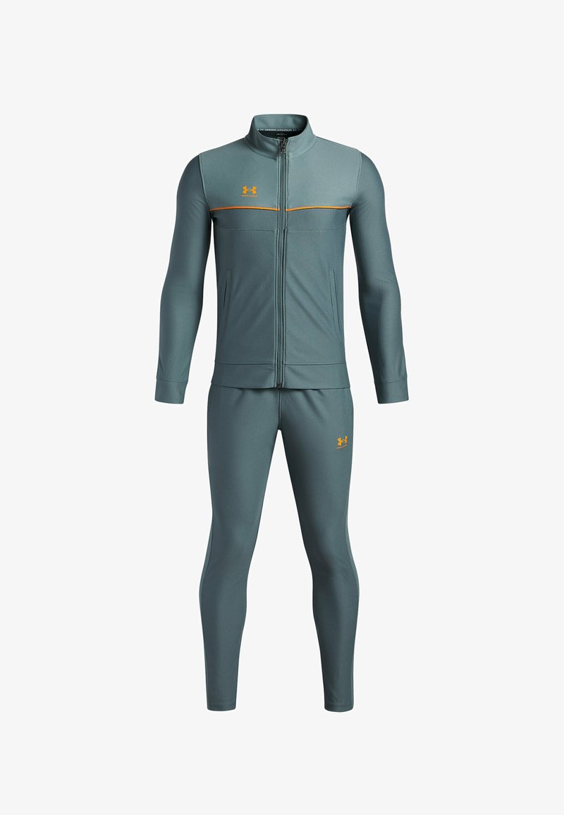 Urheilupuku tummansinisenä, jossa on vetoketjullinen takki oransseilla korostusväreillä ja logolla, yhdistettynä sopiviin housuihin. Lietekangas tuntuu sileältä.