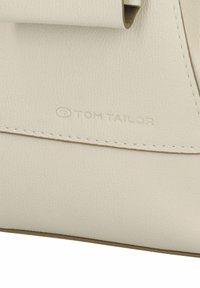 Sac à main en cuir blanc avec un rabat roulé. Inclut un logo embossé, des détails de couture subtils et une finition lisse et texturée.