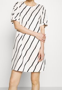 Valkoinen mekko, jossa on mustat vinoviivat, lyhyet puff-hihat, pyöreä pääntie ja rento istuvuus, valmistettu sileästä kankaasta.