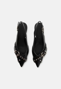 Sapatos slingback de couro preto com bicos pontiagudos, fivela decorativa e tachas metálicas ao longo da alça. Textura suave com detalhes mínimos.