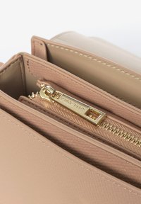 Interno di una borsa a mano in pelle beige con dettagli in cerniera dorata, texture liscia e numerosi scomparti per l'organizzazione.