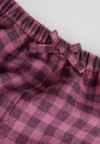 Tissu à carreaux rose et noir avec une ceinture froncée et un détail de nœud noué, présentant une texture douce et un motif tissé.