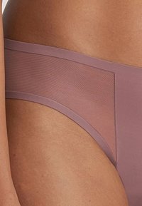 Mutande lilla chiare realizzate in un materiale morbido con un pannello trasparente su un lato. Il design presenta un elastico sottile in vita e una copertura minima.