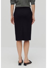 Jupe crayon noire au design épuré, longueur genou, dotée d'une fente au dos et de poches discrètes, associée à des escarpins noirs ouverts.