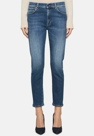 Jeans blu scuro a taglio slim, con tasche frontali, chiusura con zip e una leggera sfumatura sbiadita vicino alle cuciture; abbinati a tacchi neri.