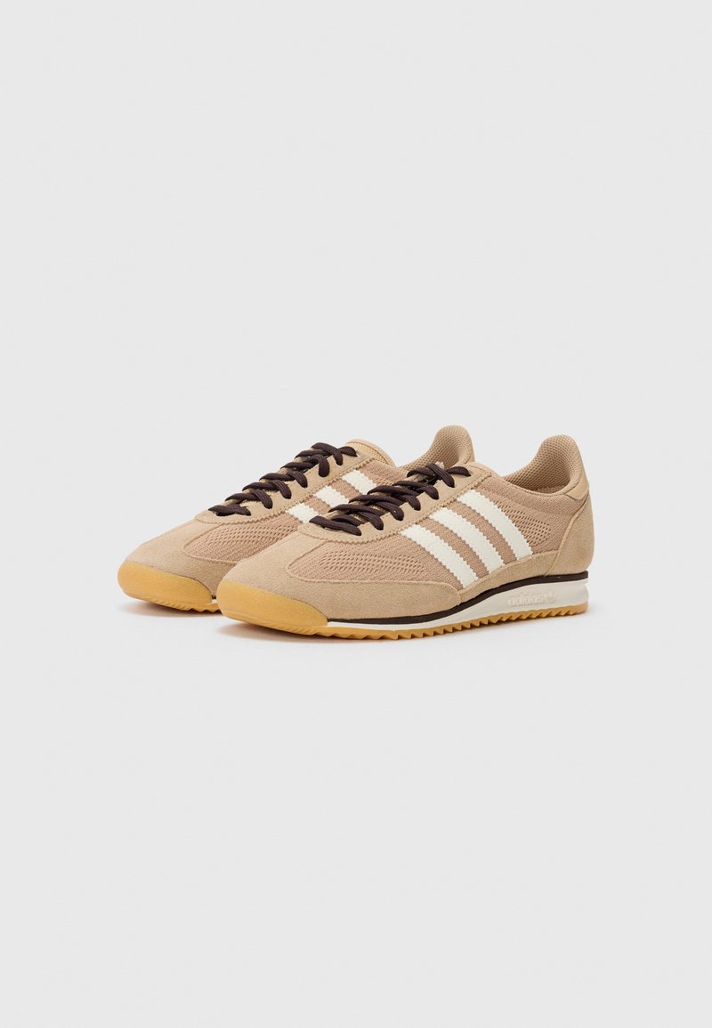 Zapatillas de serraje marrón con paneles de malla, que presentan tres franjas blancas, cordones marrones y una suela de goma con un acabado texturizado.