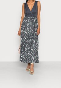 Maxi sukienka z głębokim dekoltem w kształcie litery V, ciemnoszara góra i zwiewna spódnica z wielokolorowym abstrakcyjnym wzorem. Świetliste sandały.