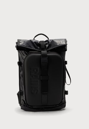 Sac à dos noir à fermeture roulante avec une grande poche avant zippée embossée du nom de la marque et une sangle de sécurisation centrale.