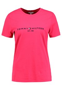 Camiseta de algodón rosa con el texto del logo en navy "TOMMY HILFIGER EST. 1985" y un pequeño gráfico de la bandera, escote redondo y mangas cortas.