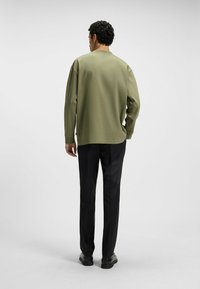 Olive green long-sleeve shirt with a crew neck, paired with black trousers, showcasing a relaxed fit and smooth fabric texture.