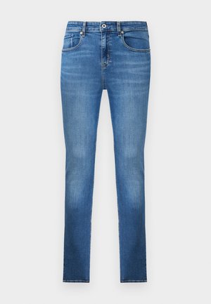 Blå slim-fit denimjeans med frontlommer, beltehemper og knappelukking, vist mot en hvit bakgrunn.