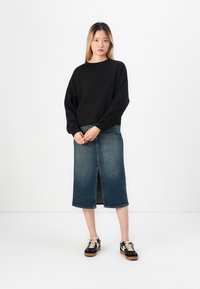 Sweatshirt noir à col rond, jupe midi en denim avec fente au devant, et baskets noires avec lacets beiges. Tenue simple et décontractée avec des éléments classiques.